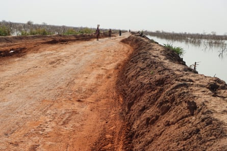 A red dirt road with raised banks and wate on either side.