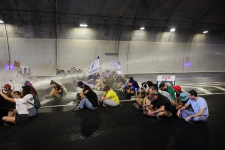 People sitting on a road in a tunnel are sprayed with jets of water