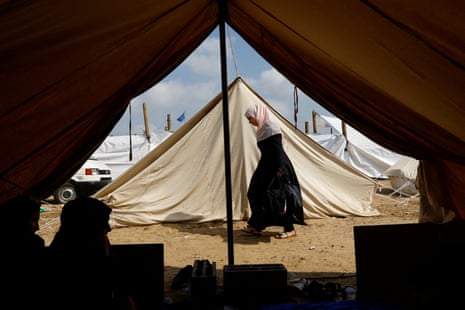 A woman walks past tents as Palestinians, who fled their houses amid Israeli strikes take shelter in a tent camp at a UN-run centre in Khan Younis.