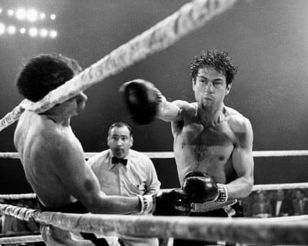 De Niro throwing a punch in the boxing ring, knocking out his opponent on the ropes as the referee looks on in Raging Bull, 1980