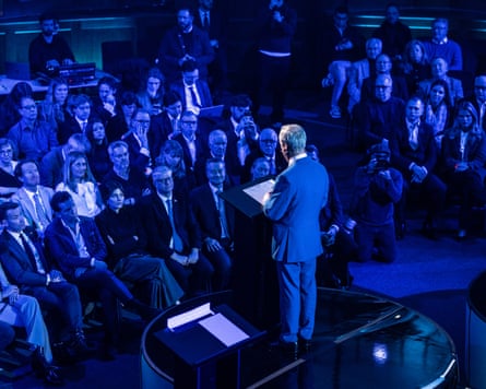 View from behind Farage of the audience sitting in blue light