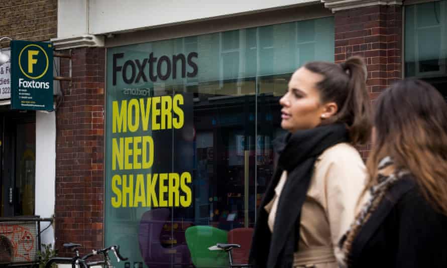 A branch of Foxtons with two women standing outside it; on the window is the slogan "Foxtons: Movers Need Shakers' in black and yellow