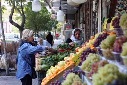 Women look at produce displayed on a stall on a street in Tehran