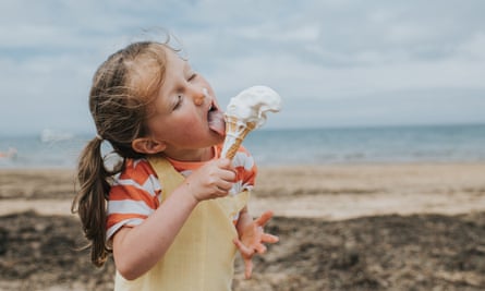 A small girl licks melting ice-cream off her cone, on the beach