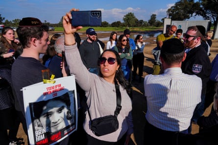 Una mujer sostiene un teléfono mientras la gente se reúne, una de ellas con un cartel de rehenes.