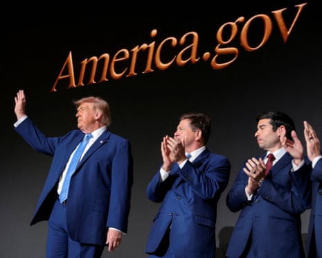 Donald Trump waves as people near him clap, under a sign for America.gov