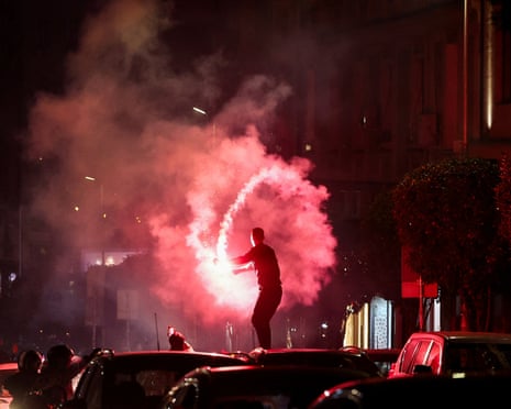 A supporter standing on a car swings a red flare amid thick smoke, celebrating election results