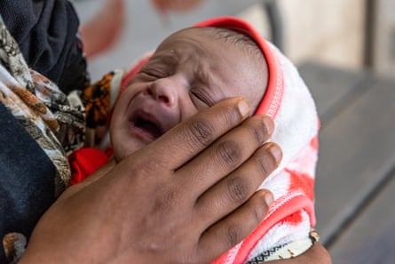 A tiny baby cries while being held by his mother
