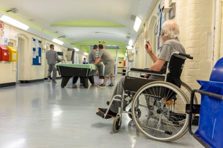 A prisoner sits in a wheelchair, watching other prisoners playing pool.