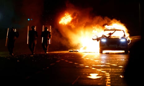 ОМОН идет рядом с горящей полицейской машиной возле места поножовщины в Дублине