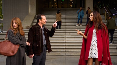 Janssen, wearing a polka-dot dress and red cloak, points at a man, who points at her in turn