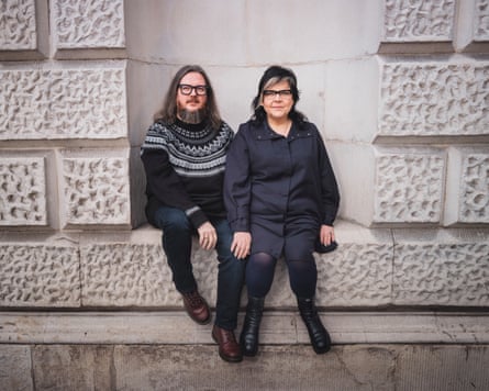 A man and a woman both dressed in black, sit on a wall.