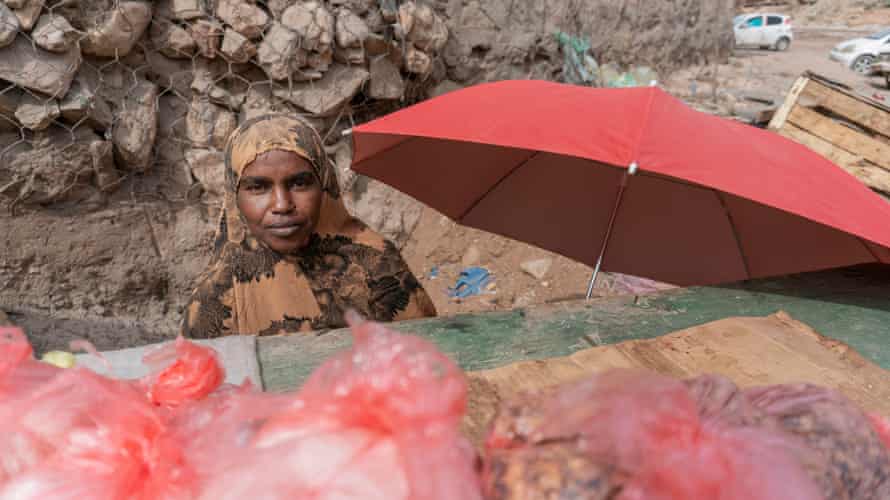Yurub Omar stands in a patterned headscarf behind a red umbrella