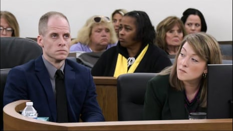Man in suit at long table in court next to woman in business attire.