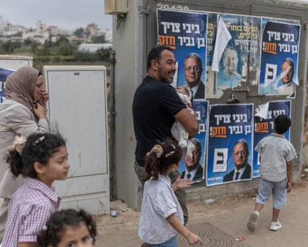 A Palestinian family walk past campaign posters for Itamar Ben-Gvir