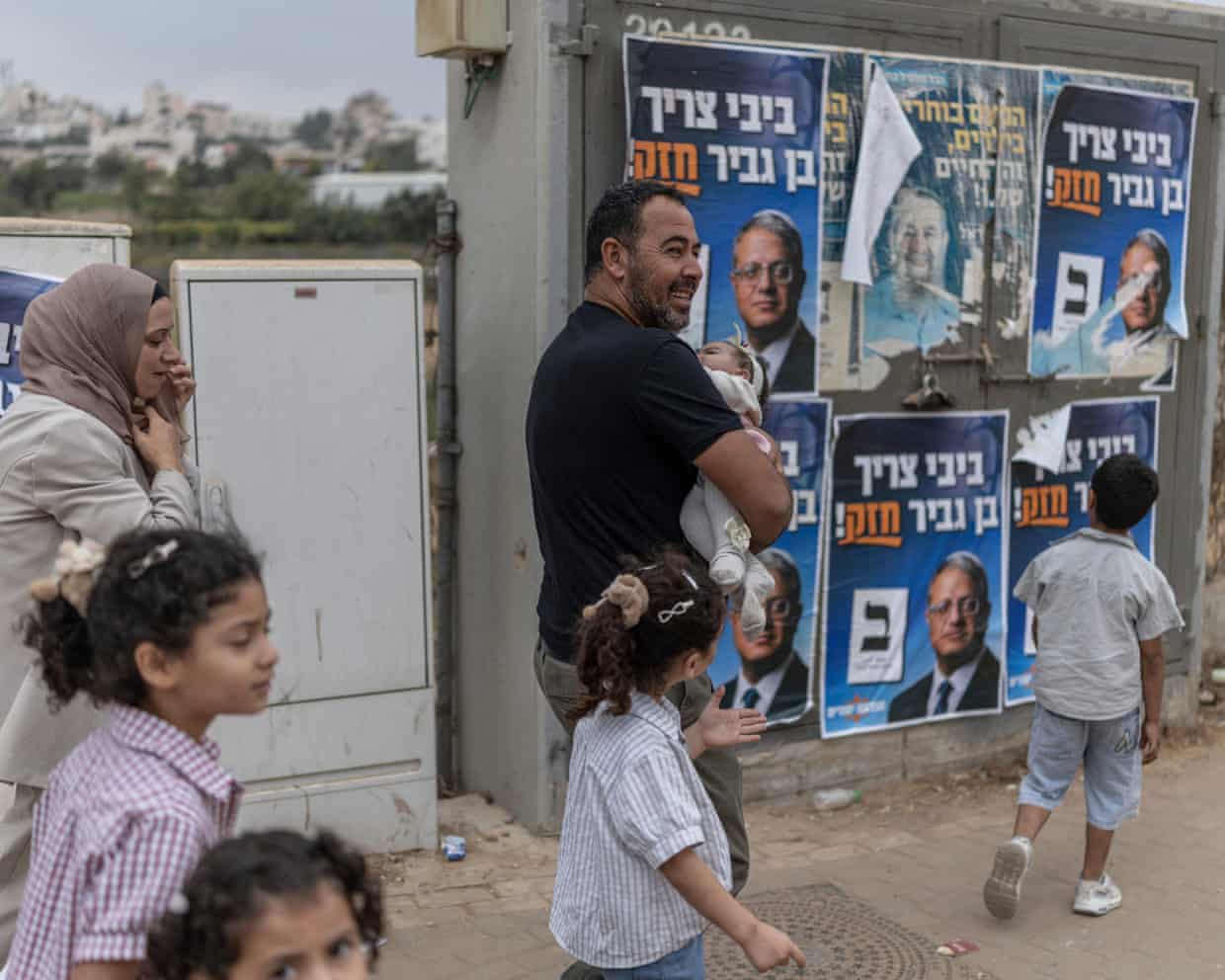 A Palestinian family walk past campaign posters for Itamar Ben-Gvir