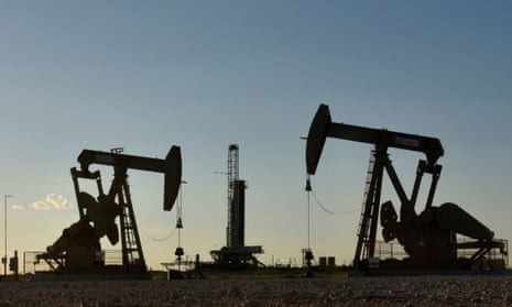 Pump jacks operate in front of a drilling rig in an oil field in Midland, Texas