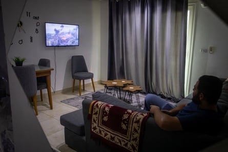 Sami Abu Tabaq sits alone in his apartment in Cairo, Egypt, while his fiancee remains in Gaza. Images of Gaza are shown on the television.