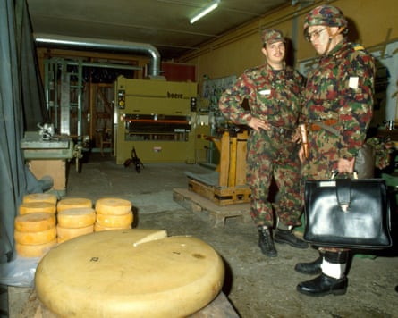 Two men in fatigues stand in a bunker. One is staring at an enormous wheel of cheese, the other merely glancing at it.
