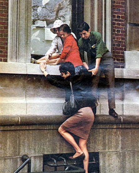 A woman scaling the side of a building, helped by three other people.