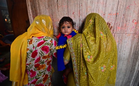 Two women turning away from the camera, with. child in between, looking at the camera, wearing bright colours