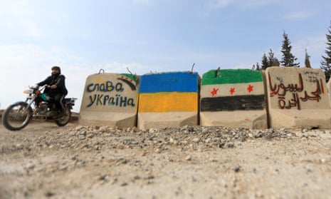 A man rides a motorcycle past cement blocks painted with flags of Ukraine (left) and the Syrian opposition near the Syrian rebel-held city of al-Bab in northern Aleppo. Inscriptions beside the flags read, in Cyrillic, ‘Glory to Ukraine’ and, in Arabic, ‘Glory to free Syria’.