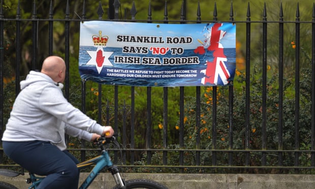 A cyclist passes a banner protesting against the Northern Ireland protocol on Belfast’s Shankill Road. Northern Ireland,Brexit,Democratic Unionist party,Edwin Poots,David Campbell,harbouchnews