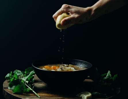 Person squeezing lemon on soup in a black bowl