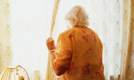 An elderly woman looks out from her home.