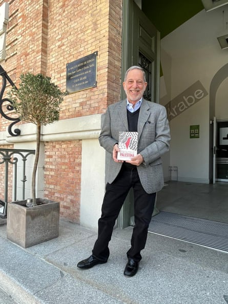 smiling man holds book in doorway. the word ‘palestina’ is visible on the cover