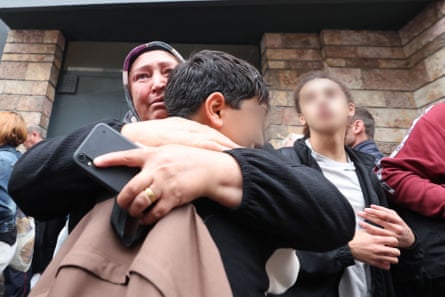 A woman hugs a boy among people waiting outside the school