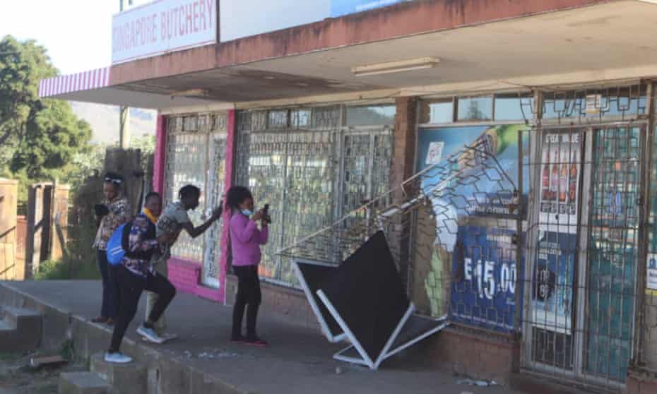 People take pictures of a damaged shop in Mbabane, Eswatini, following protests. 