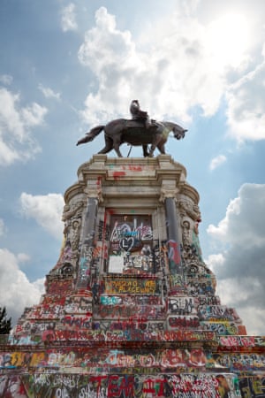 Monument of Robert E Lee riding a horse atop a pillar that is covered in BLM graffiti