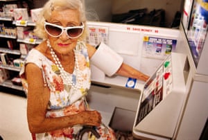 an older woman in a sleeveless dress and large flared white sunglasses with her arm in a blood pressure machine at a pharmacy