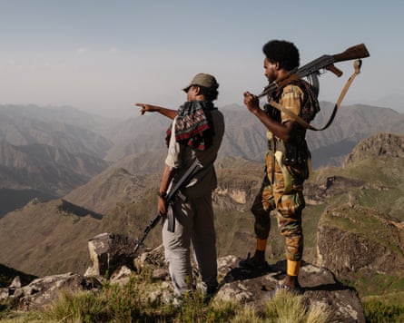 Two men with guns look out over mountains