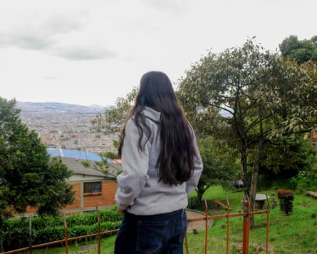A girl with long dark hair and wearing jeans and a grey hoodie, stands with her back to the camera