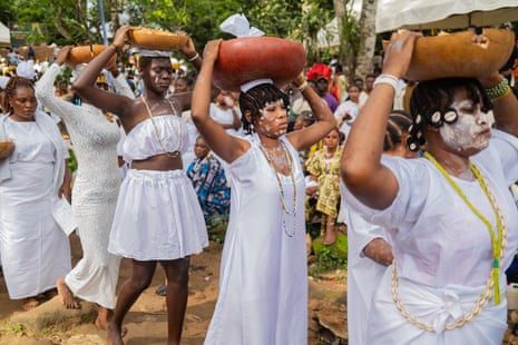 A line of African women wearing white dresses with bowls on their head