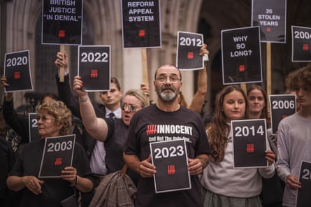 A man outside court surrounded by people holding placards with years on and statements such as ‘why so long?’