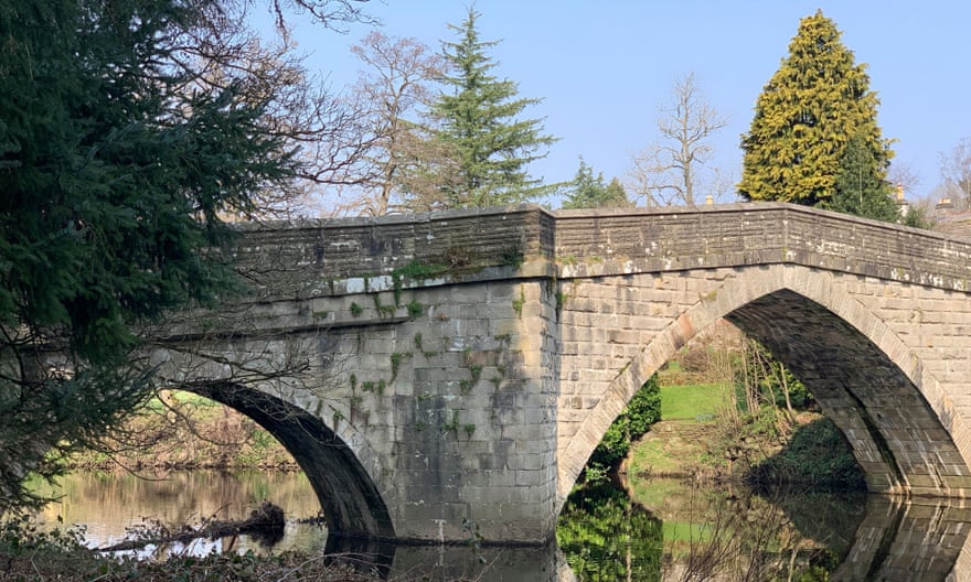 Brick Frogatt Bridge, with two arches and trees nearby, over the very still River Derwent