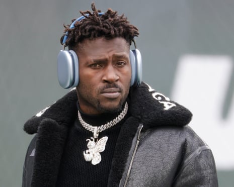 Antonio Brown wears large silver headphones and a diamond chain, looking off to the side