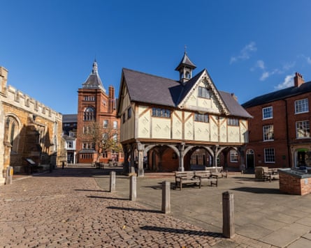 A historic paved square with a stilted medieval building, a church, a red-brick Georgian building and a red-brick Victorian building with a turret