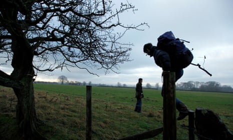 Two ramblers cross a fence in a field in Penrith and the Border