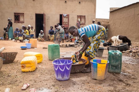 A girl washes clothes as families stand outside a school used as a shelter for internally displaced people in Burkina Faso in June 2019.