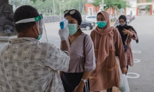 An officer checks body temperature of tourists before entering Bukit Cinta, Central Java.