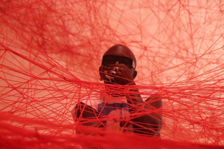 A man stands within a dense web of red string.