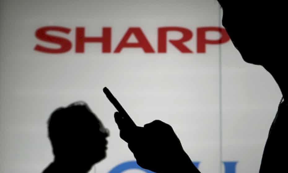 Man using his mobile phone as he walks past a logo of Sharp Corp