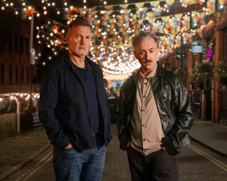 Two men standing on a street with lights and bunting down it.