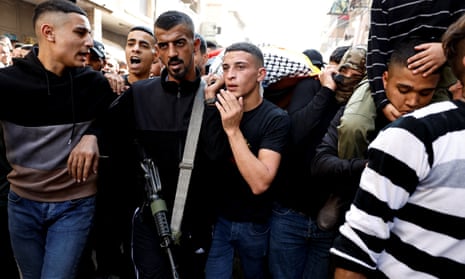 A crowd of young Palestinian men, including one armed with an assault rifle