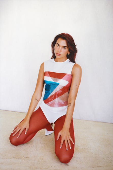 Dua Lipa crouching on the floor wearing a white, blue and red bodysuit and red tights