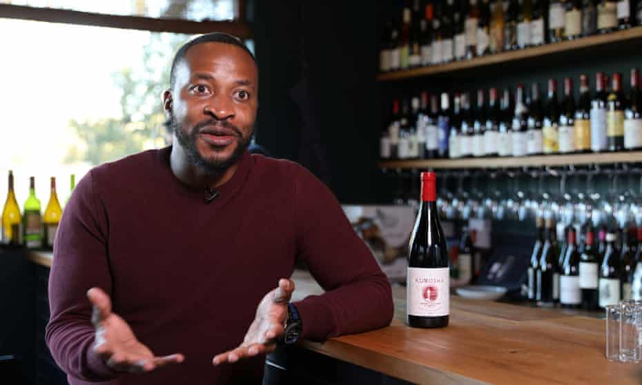 A Zimbabwean man sits at a bar with shelves of wine bottles behind him